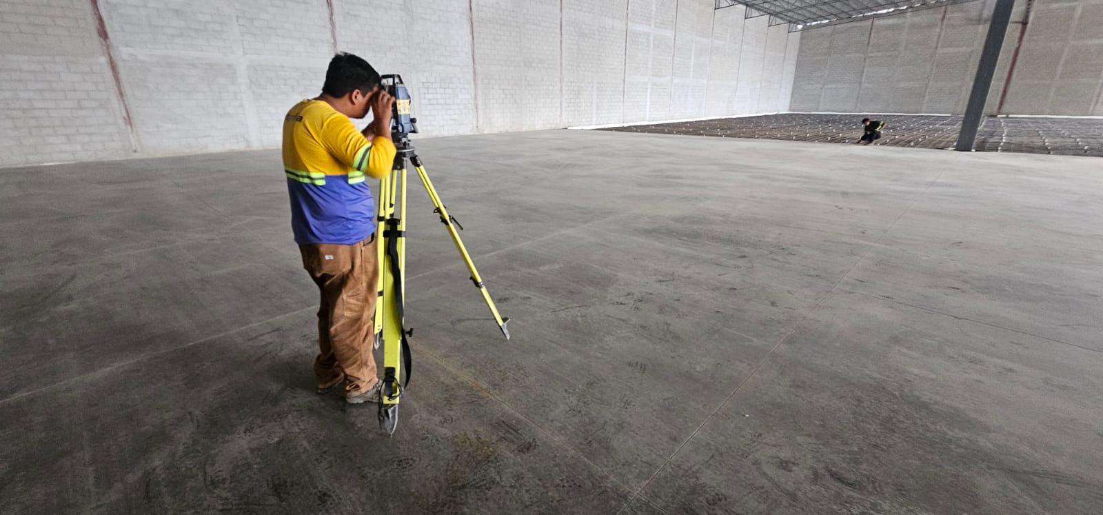 Topógrafo realizando control de nivel en el piso de una nave industrial